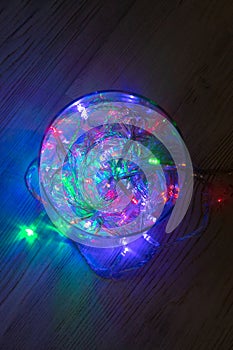 Christmas multicolored red green blue garland lights from LED bulbs in glass jar on wooden table background. Top view, vertical