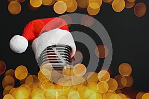 Christmas music. Microphone with Santa hat on black background, bokeh effect