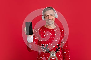 Christmas music. Santa with phone and headphone. Man in Christmas santa sweater, winter holiday, christmas background.