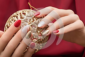 Christmas nail design. Female hands with red and golden manicure. Female hold golden xmas toy orb. New Year decoration