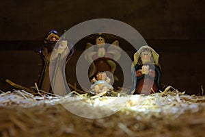 Christmas nativity scene of baby Jesus in the manger over straw. Infant Jesus, Angel, virgin Mary and Joseph colored figurines