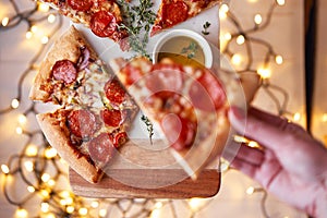 Christmas and New Year atmosphere. Womans hand takes slice of Italian pizza with melting tomato, pepperoni and cheese on