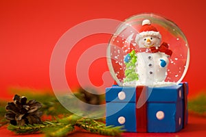 Christmas and new year card with snow globe snowman inside. Gift box on red background. Holidays, winter and celebration concept.