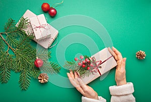 Christmas or New Year celebration green paper festive background with female hands holding wrapped gift box, decoration