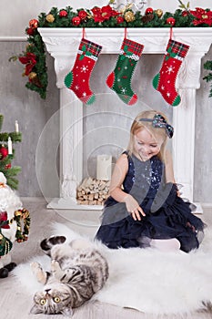 Christmas or New year celebration. Happy holidays. Little girl playing with cat near Christmas tree and fireplace with christmas s