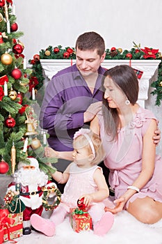 Christmas or New year celebration. Happy young family sitting in chair near Christmas tree with xmas gifts. A fireplace with chris