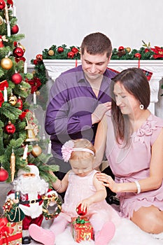 Christmas or New year celebration. Happy young family sitting in chair near Christmas tree with xmas gifts. A fireplace with chris