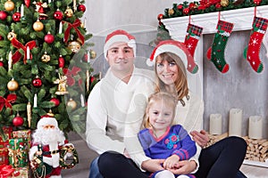 Christmas or New year celebration. Happy young family sitting near Christmas tree with xmas gifts. A fireplace with christmas stoc