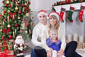 Christmas or New year celebration. Happy young family sitting near Christmas tree with xmas gifts. A fireplace with christmas stoc