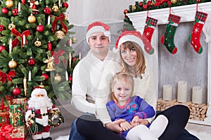 Christmas or New year celebration. Happy young family sitting near Christmas tree with xmas gifts. A fireplace with christmas stoc