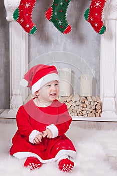Christmas or New year celebration. Little girl dressed in a red festive suit of gnome and santa hat, sits on the floor near Christ