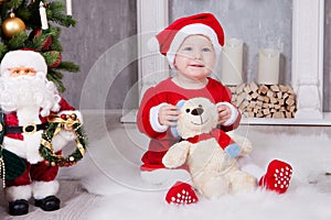 Christmas or New year celebration. Little girl in red dress and santa hat with bear toy sitting on the floor near the Christmas tr