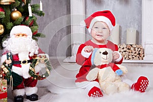 Christmas or New year celebration. Little girl in red dress and santa hat with bear toy sitting on the floor near the Christmas tr