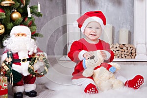 Christmas or New year celebration. Little girl in red dress and santa hat with bear toy sitting on the floor near the Christmas tr