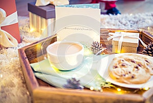Christmas and New Year composition. Cocoa, cookies, little giftbox and postcard on the wooden tray with xmas background. Sweets