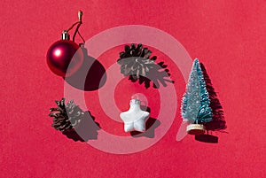 Christmas, New Year concept flat lay with festive toys and pine cones on the red sunny background.