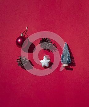Christmas, New Year concept flat lay with festive toys and pine cones on the red sunny background.