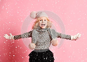 Christmas and New Year concept. Screaming baby girl in warm hat and gloves standing under snow with hands spread up