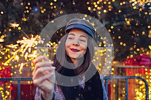 Christmas, New Year concept. Woman burning sparkler by Christmas tree on city street fair