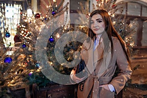 Christmas, New Year concept. Woman walking on city street by decorated trees. Stylish girl enjoying holiday atmosphere