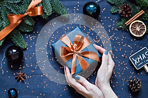 Christmas, New Year dark blue flat lay. Woman`s hands hold a gift.