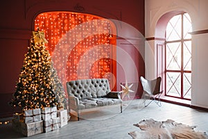 Christmas and New Year decorated interior room with light bokeh garland and New year tree and classic grey sofa in front of red