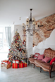 Christmas and New Year decorated interior room with red presents and New year tree and classic brown sofa in front of white wall.