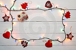 Christmas or New Year decoration with copy space. Frame made from Christmas garland lights and red textile baubles on white wooden