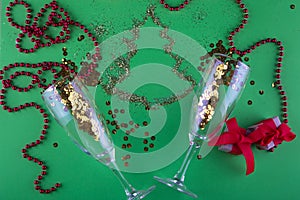 Christmas, New year flatly. Two wine glasses with sparkles inside lay on green background near pine tree made of golden glitter,