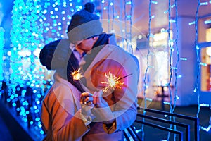 Christmas and New year fun concept. Couple in love burning sparklers by holiday illumination outdoors. Festive holidays