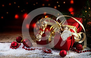 christmas and new year gift in red paper, golden ribbons and baubles a rustic wooden board with snow, dark background with