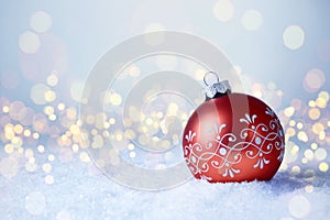 Christmas and New Year greeting card. Holiday ornament, winter decoration. Red christmas ball in snow over bokeh lights background