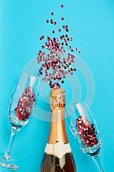 Christmas and New Year or holiday festive card. Bottle of champagne, glasses and pink sparkles over blue background
