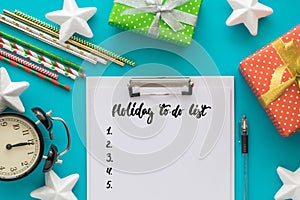 Christmas and New Year holiday to do list with notepad, pen, gift boxes, clock, cocktail tubes, stars on the blue