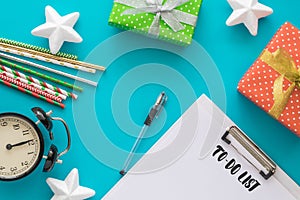 Christmas and New Year holiday to do list with notepad, pen, gift boxes, clock, cocktail tubes, stars on the blue