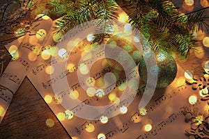 Christmas and New Year music. Fir tree branch, festive balls and music sheets on wooden background, bokeh effect