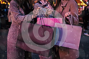 Christmas and New Year presents. Women friends holding paper bags after shopping on street fair under snow