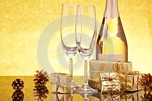 Christmas and New Year still life: golden gift boxes, champagne bottle and empty champagne flutes on festive gold background
