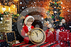 Christmas or New Year time. Cute child in santa claus hat holding red alarm clock with thumb up. Twelve O`clock midnight