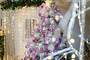 Christmas or New Year tree decorated with purple baubles, shiny star on top and garland lights with two white lanterns