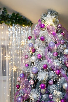 Christmas or New Year tree decorated with purple baubles, shiny star on top and garland lights with two white lanterns