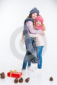Christmas. New Year. Two little sisters holding present in winter clothes. Pink and grey hats and scarfs. Family. Winter