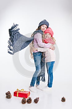 Christmas. New Year. Two little sisters holding present in winter clothes. Pink and grey hats and scarfs. Family. Winter