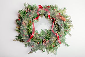 Christmas and New Year wreath made of fir, pine evergreen branches, rose hips, cones decorated with red ribbon bow.