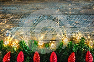 Christmas New Years greeting card poster fir tree branches golden sparkling garland lights red pine cones on rustic wood