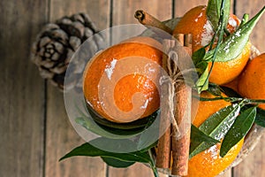 Christmas New Years greeting card poster with fresh raw tangerines on stem with green leaves cinnamon stick in box pine cone