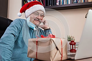 Christmas online congratulation. Senior man in santa claus hat talks using laptop for video call friends and childrens. The room