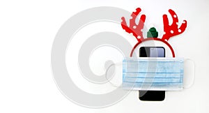 Christmas online shopping and communicate. Smartphone with antlers and medical mask on white background. Top view, banner with