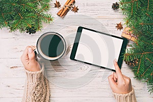 Christmas online shopping. Female hand touch screen of tablet, top view on wooden bakground, copy space and holding mug of coffee