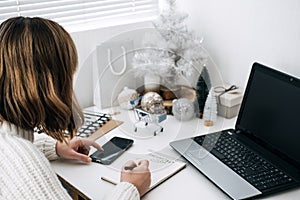 Christmas online shopping, winter sale, black Friday. Woman with shopping list, smartphone and laptop having shopping